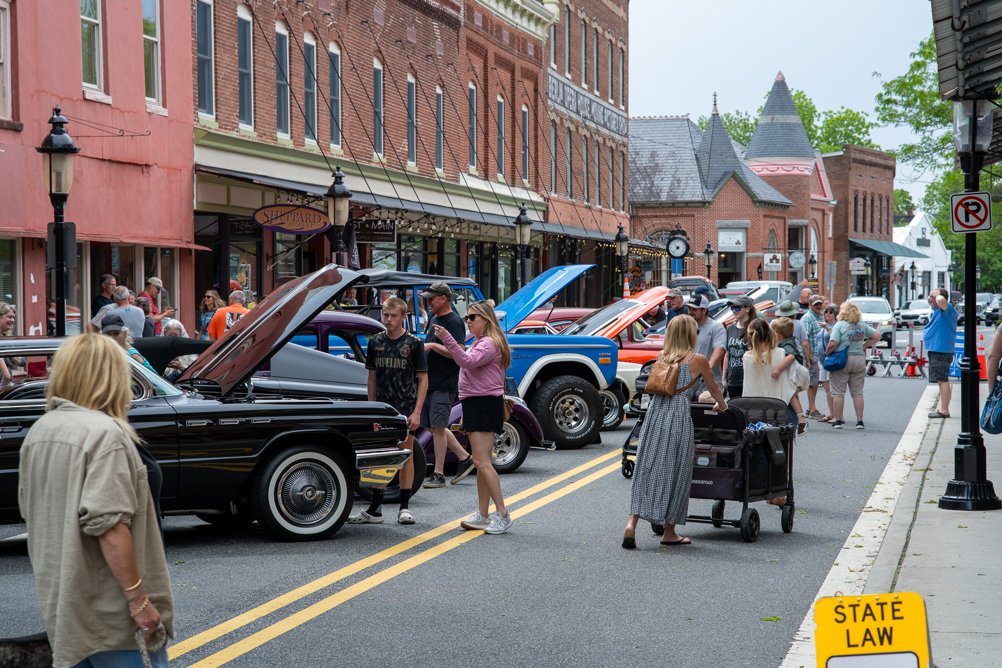a crowd of people walking down a street next to parked cars